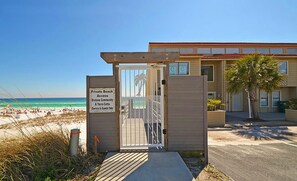 Une entrée fermée par un portail donnant accès à une plage privée, d’où l’on a une vue dégagée sur l’océan, avec un bâtiment visible au loin.