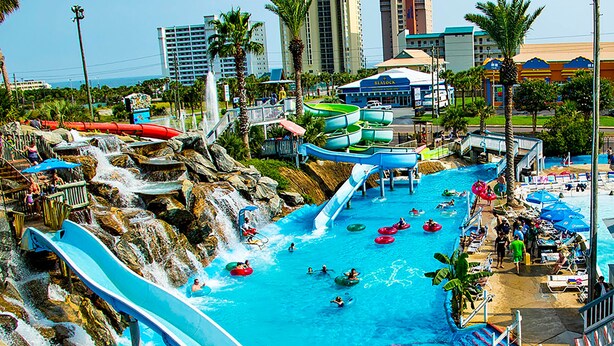 Parque acuático con múltiples toboganes y piscinas, rodeado de palmeras y edificios.