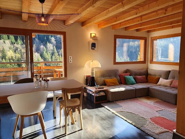 A cozy cabin interior with a dining area, a sofa, and large windows offering a forest view.