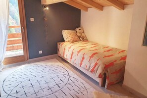 A small bedroom with a bed, a window, and a wall-mounted light.