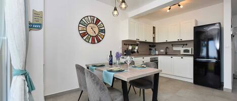 Une cuisine moderne avec des meubles blancs, un réfrigérateur noir et un coin repas avec une table mise pour deux personnes.