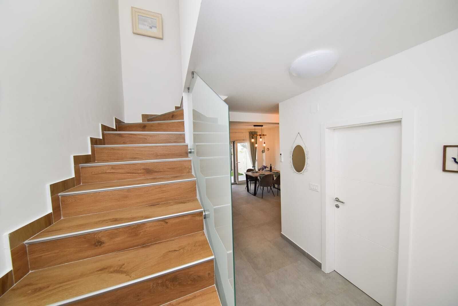 Eine Treppe mit Holzdielen und einer Glastrennwand führt zu einem Essbereich mit Tisch und Stühlen.