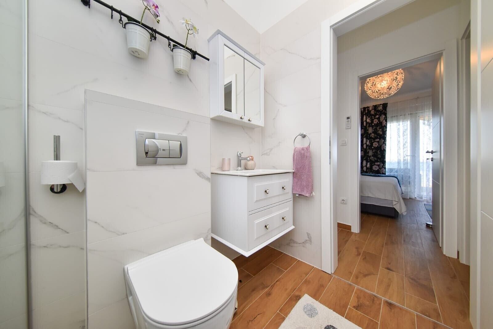 A modern bathroom with a toilet, sink, and mirror. There is a shower area with a glass door and a wooden floor.