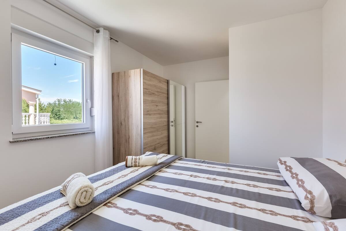 A bedroom with a bed, a window with a view, a wardrobe, and a door.