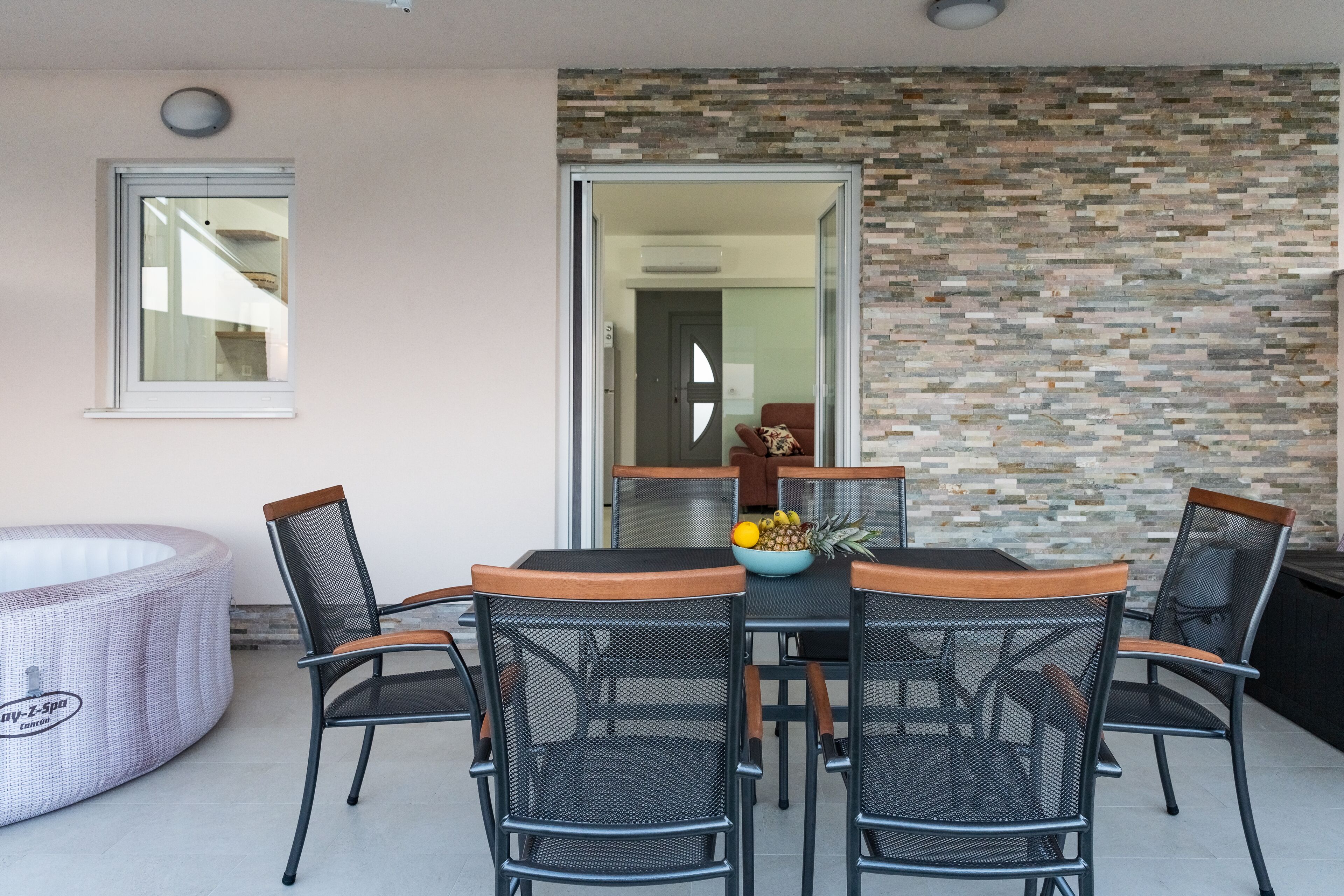 A dining area with a table and chairs, a hot tub, and a stone wall.