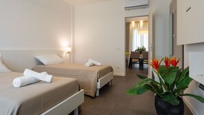 Ein Hotelzimmer mit zwei Betten, einer großen Topfpflanze und Blick auf den Flur.