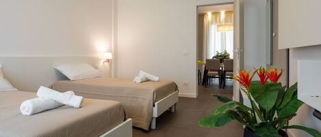 A hotel room with two beds, a large potted plant, and a view of the hallway.