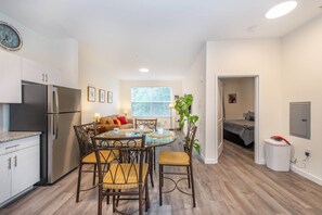 Cocina compacta con electrodomésticos modernos, comedor con mesa redonda y sillas, y sala de estar acogedora con sofá y ventana grande.