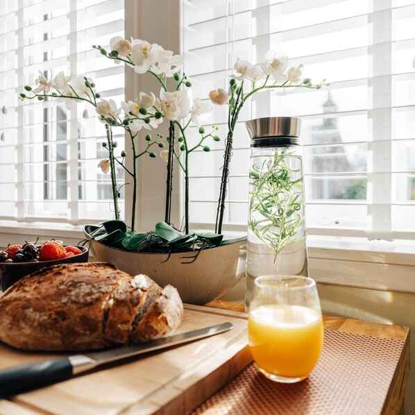 A breakfast setting with a loaf of bread, a glass of orange juice, a bowl of strawberries, and a potted plant with white flowers.