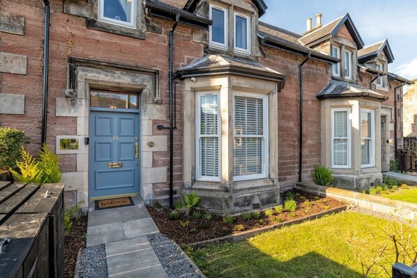 A brick house with a blue door, a bay window, and a small garden.