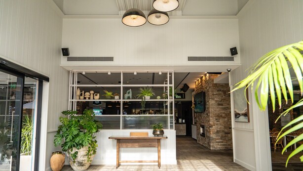 Un espace d’accueil avec un banc en bois, des plantes en pot et une vue sur le restaurant.