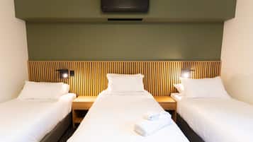 Una habitación de hotel con dos camas individuales, cabecera de madera, mesitas de noche con lámparas y aire acondicionado instalado en la pared.