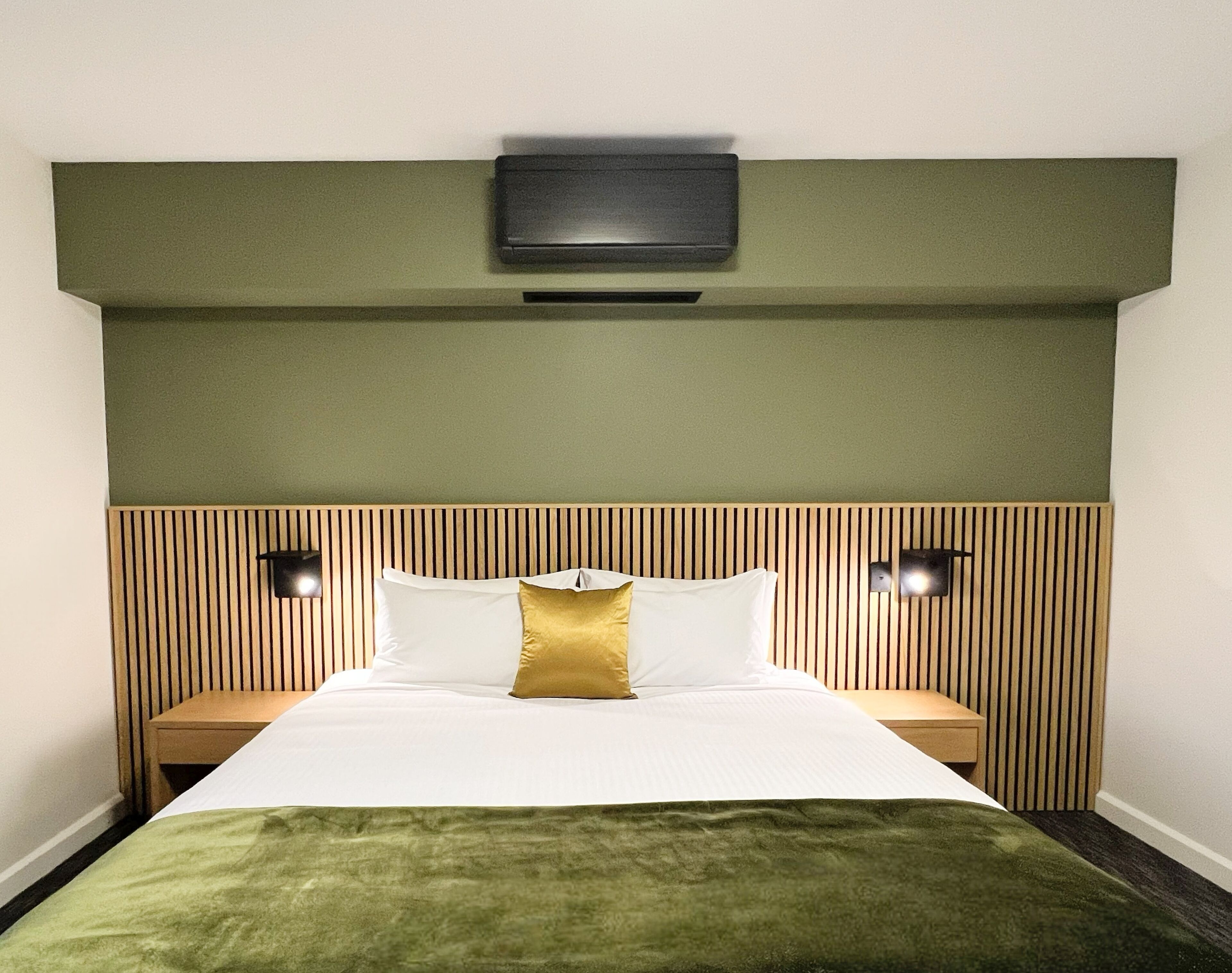 Une chambre d’hôtel avec un lit, deux tables de chevet, un téléviseur fixé au mur et une tête de lit verte.