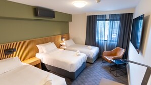 Une chambre d’hôtel avec deux lits, un bureau, une chaise, une télévision et une fenêtre avec des rideaux.