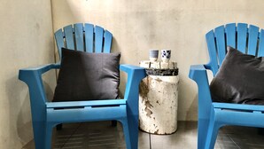 Zwei blaue Stühle mit dunklen Kissen, ein kleiner weißer Tisch mit einem dekorativen Gegenstand und eine schlichte Wand.