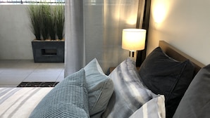 Ein modernes Schlafzimmer mit einem Bett, Kissen, einem Nachttisch, einer Lampe und einer Topfpflanze.