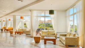 A spacious lobby with multiple seating areas, large windows, and a modern chandelier. - Aeolian Village Beach Resort (Lesvos)