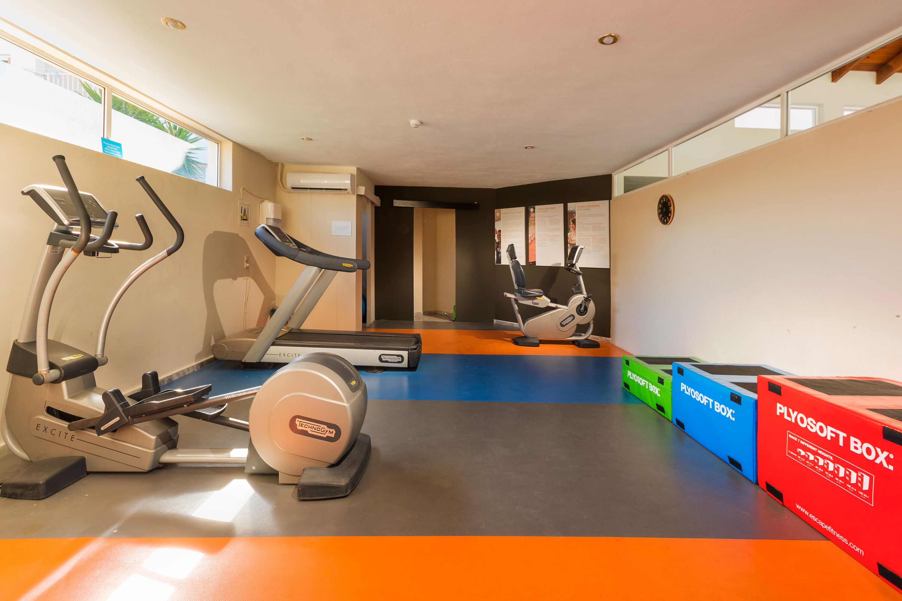 A gym with treadmills, stationary bikes, and exercise equipment. There are PlyoSoft boxes and a blue mat on the floor.