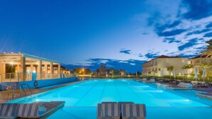 A swimming pool with lounge chairs and a building with multiple floors and balconies. - Aeolian Village Beach Resort (Lesvos)