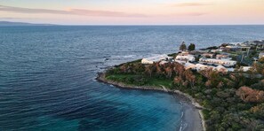 An aerial view of a coastal residential area with houses along the shoreline, surrounded by dense vegetation and a clear view of the ocean. - Windspray  – ocean views from kitchen and living (Culburra Beach)