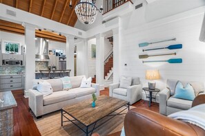 Un vaste salon doté d’un plafond en bois, une cuisine à l’arrière-plan et un escalier menant à l’étage supérieur.