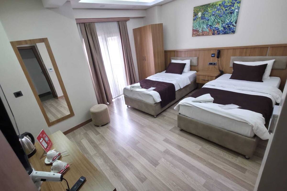 Ein Hotelzimmer mit zwei Betten, einem Schreibtisch mit Stuhl, einem Spiegel und einem Bild an der Wand.