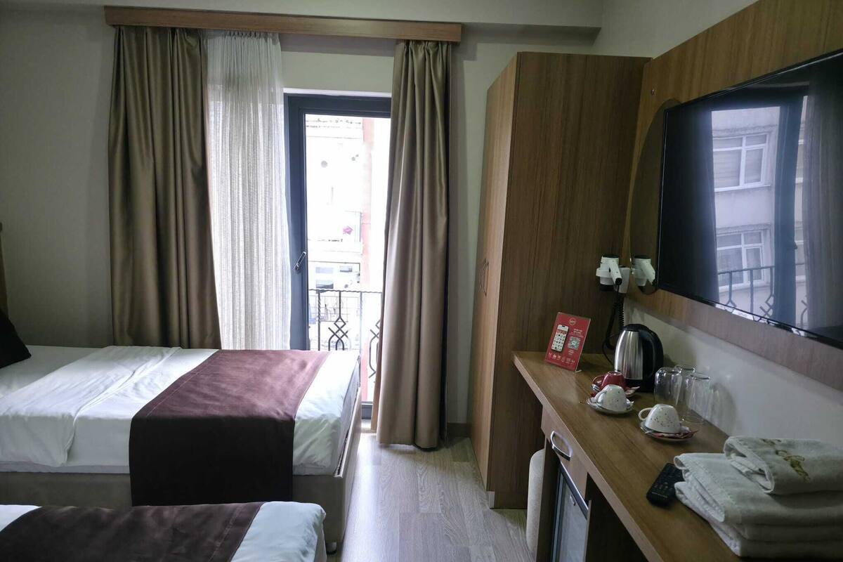 Ein Hotelzimmer mit zwei Betten, einem Schreibtisch mit Telefon, einem Spiegel und einem Fenster mit Vorhängen.