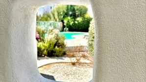 Vista a través d'una finestra amb relleu, on es veu una piscina i vegetació.
