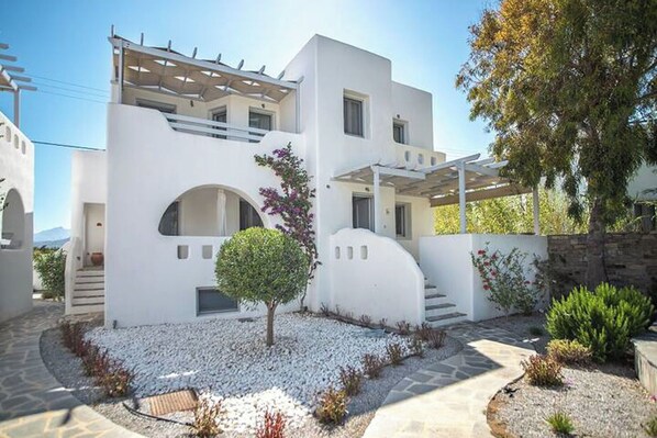 A modern white building with a covered patio, a small tree, and a stone pathway. - A Perfect Home In Naxos (Stelida)