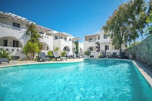 A swimming pool with lounge chairs, surrounded by white buildings with arches and greenery. - A Perfect Home In Naxos (Stelida)