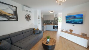 A modern living room with a grey sofa, a round coffee table with a plant, and a kitchen in the background. - Apartments Adela I (Novalja)