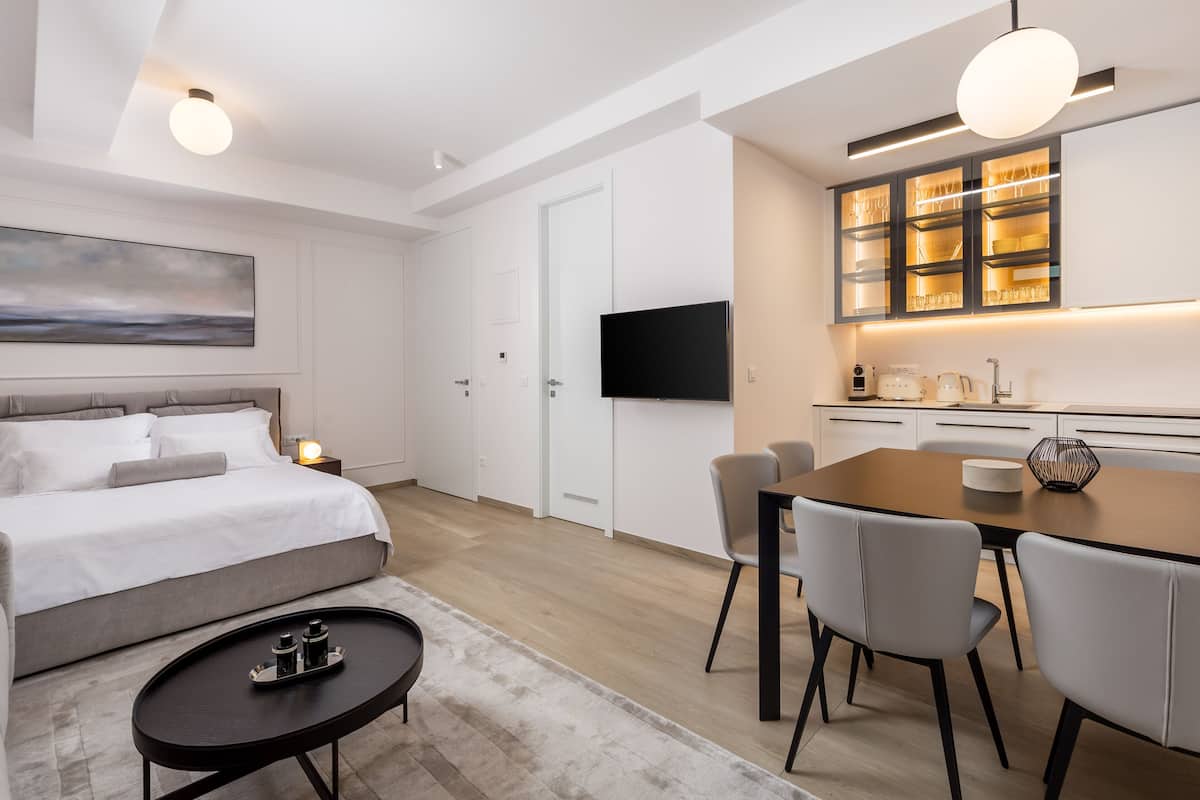 A modern hotel room with a bed, bedside table, and a dining area with chairs and a table.