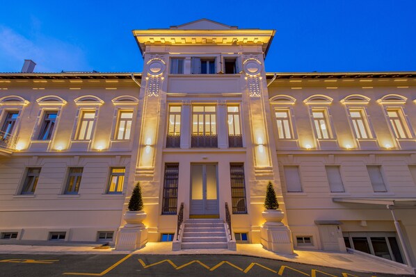 Ein prächtiges Gebäude mit einer symmetrischen Fassade, großen Fenstern und einem zentralen Eingang mit Stufen.