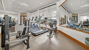 Une salle de sport moderne équipée de machines de cardio, d’appareils de musculation et de grands miroirs.