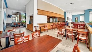 Un hall d’hôtel moderne doté d’un vaste espace salon, d’un bar et d’une cuisine visible au fond.