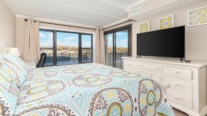Ein Schlafzimmer mit einem großen Bett, einem Fernseher, einem Schminktisch und einem Balkon mit Blick auf die Landschaft.