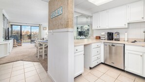 Una cocina moderna con armarios blancos, lavavajillas y comedor con mesa y sillas.