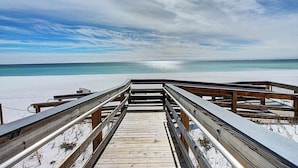 Een houten looppad dat naar een strand leidt, met heldere lucht en rustig water.