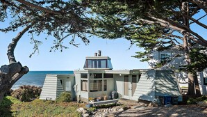 Une maison située sur la côte, avec vue sur l’océan, une petite terrasse et une allée gravillonnée.