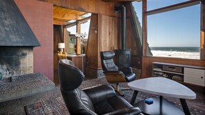 Une pièce avec une cheminée, deux fauteuils en cuir, une petite table et une vue sur la plage.