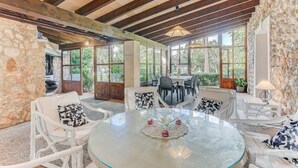 A spacious dining area with a round glass table, white wicker chairs, and a stone wall. - El Ranchon by Rentallorca (Port de Pollença)