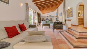 A spacious living room with a high ceiling, a sofa with red cushions, a coffee table, and a staircase leading to an upper level. - El Ranchon by Rentallorca (Port de Pollença)