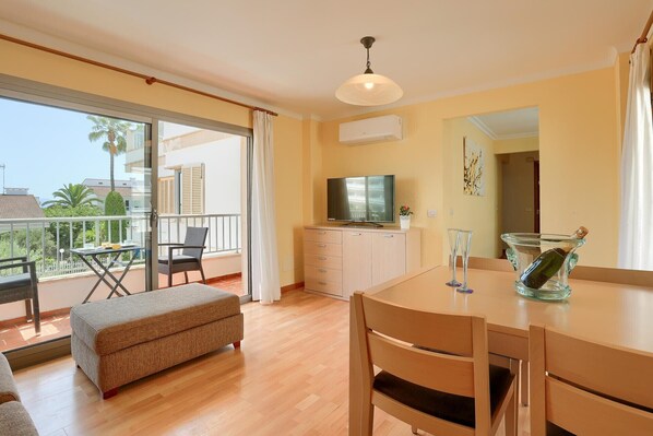 A modern living room with a balcony, a dining area, and a TV on a cabinet.