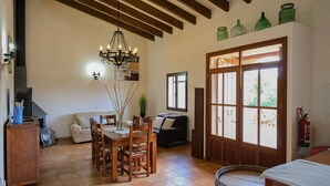 Un comedor con mesa y sillas de madera, una araña y un ventanal con vistas a la vegetación.