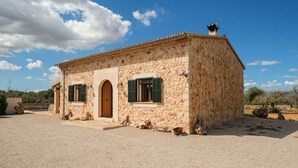 Un edificio de piedra con puerta de madera y contraventanas verdes, un camino de grava y un cielo azul despejado.