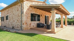 Un edificio rústico de piedra con un porche cubierto, mobiliario exterior y una antena parabólica.