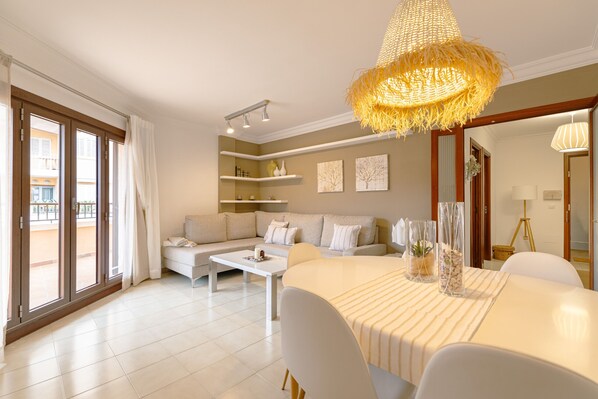 Uma sala de estar espaçosa com sofá, mesa de jantar e uma janela grande com cortinas.