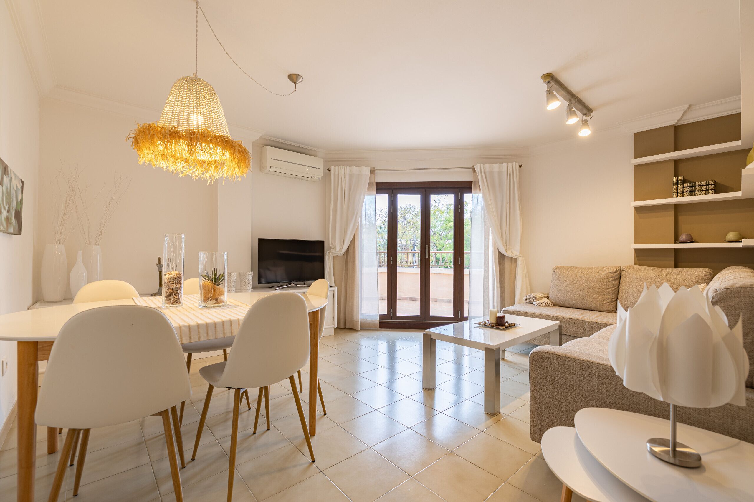 A modern living room with a dining area, a sofa, a TV, and a large window with curtains.