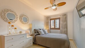 A bedroom with a bed, a dresser, two wall mirrors, a ceiling fan, and a window with curtains.
