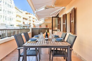 Uma área de refeições com mesa posta para quatro pessoas, cadeiras externas e uma garrafa de champanhe.